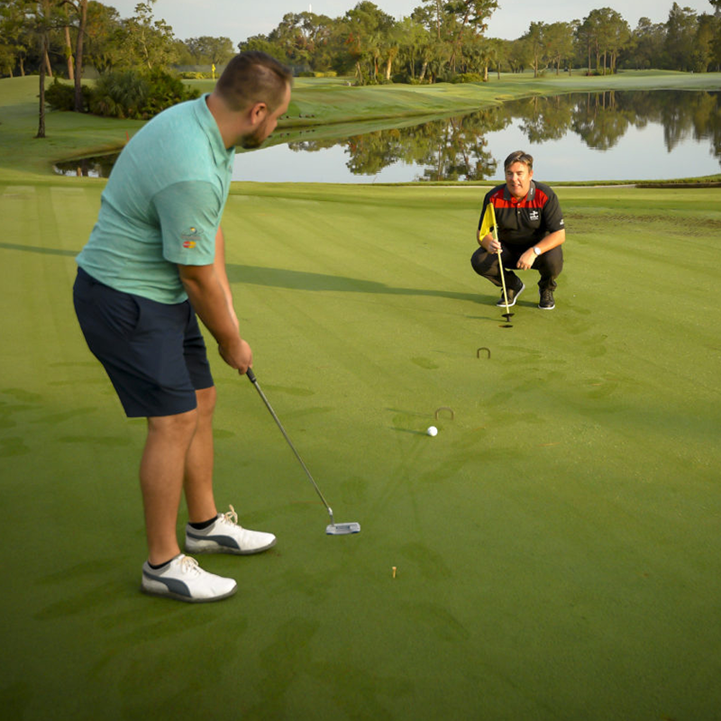 Private golf lesson of golfer swinging on green with instructor