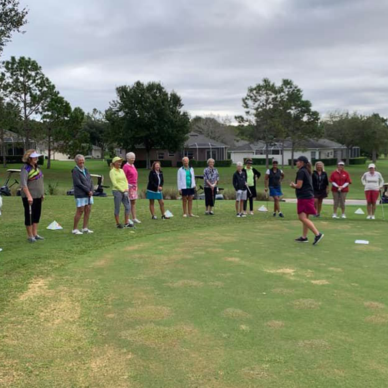 Large group of golfers receiving instruction on green